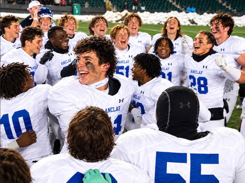 A high school football team huddled together celebrating on the field after a win